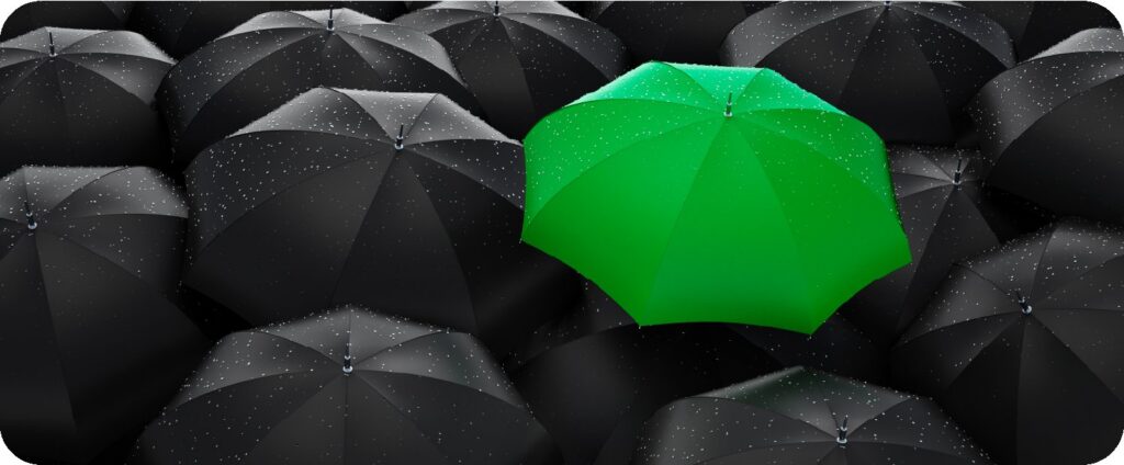 Single green umbrella standing out in a crowd of black umbrellas